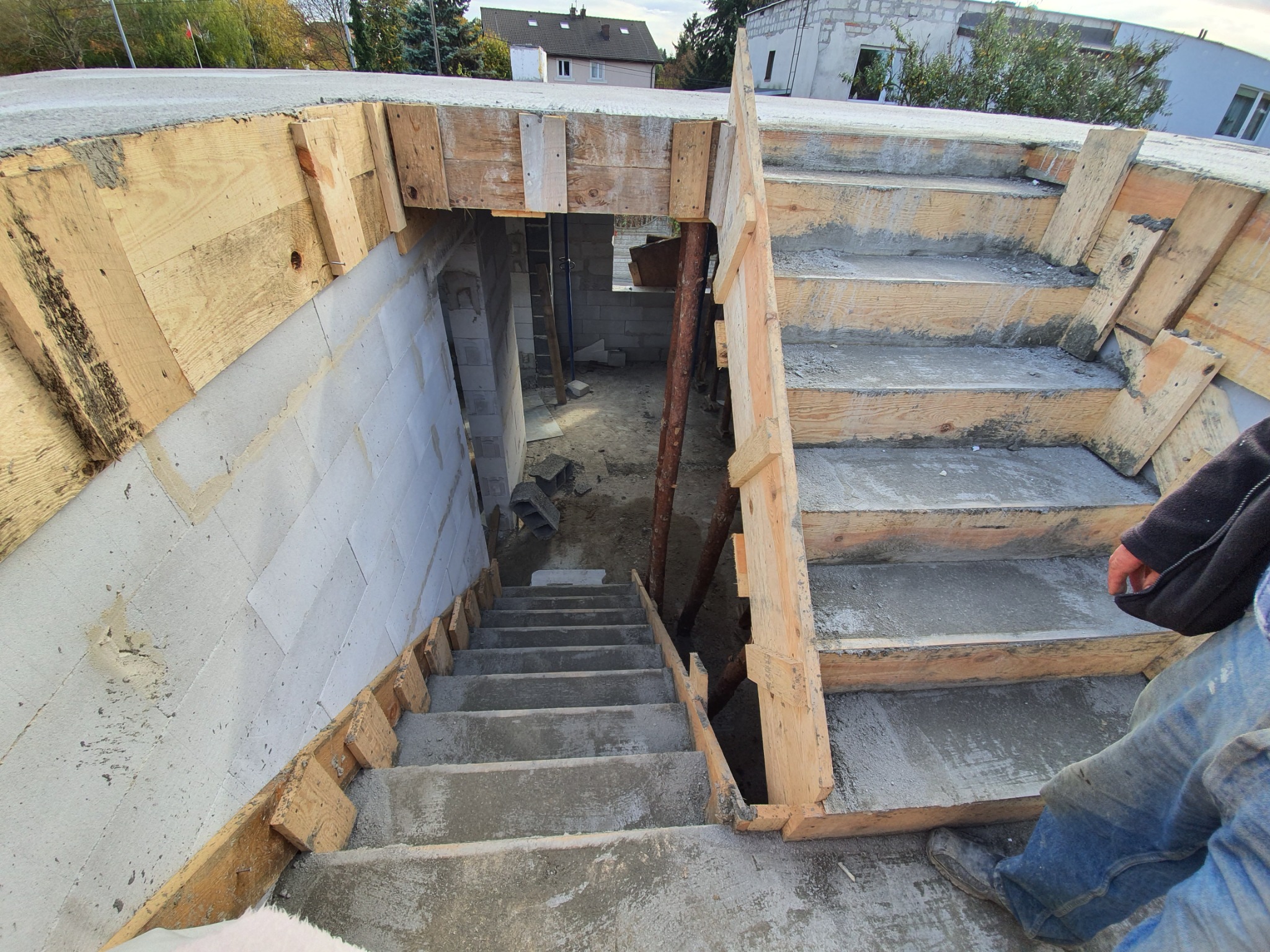 Betonowe schody w trakcie budowy, z drewnianym szalunkiem, prowadzące do piwnicy w bloku z betonu komórkowego.