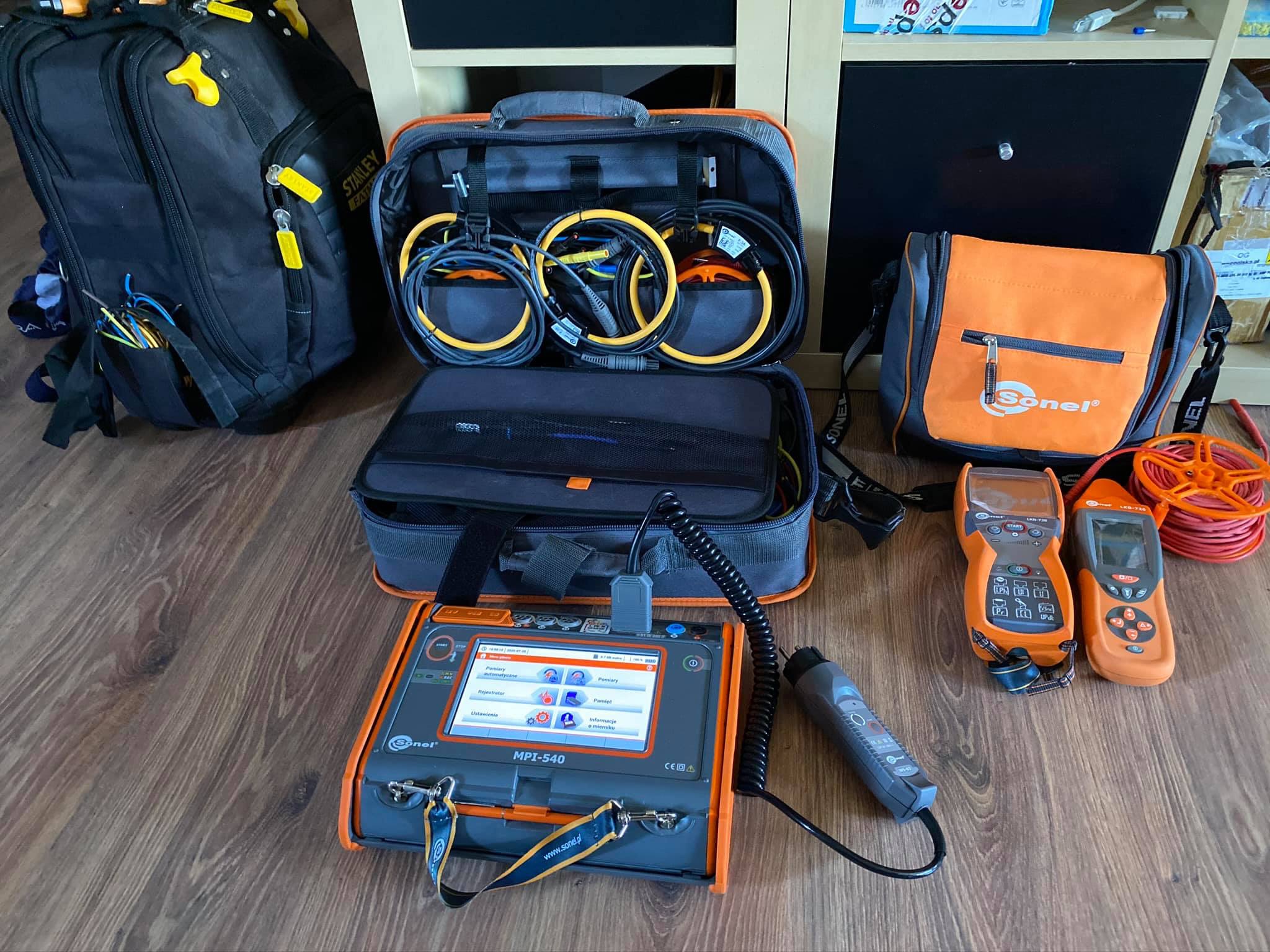 Sprzęt pomiarowy firmy Sonel: miernik wielofunkcyjny MPI-540, lokalizatory LKO-720 i LKN-730, przewody pomiarowe w torbie, plecak narzędziowy Stanley Fatmax, torba narzędziowa Sonel na podłodze...