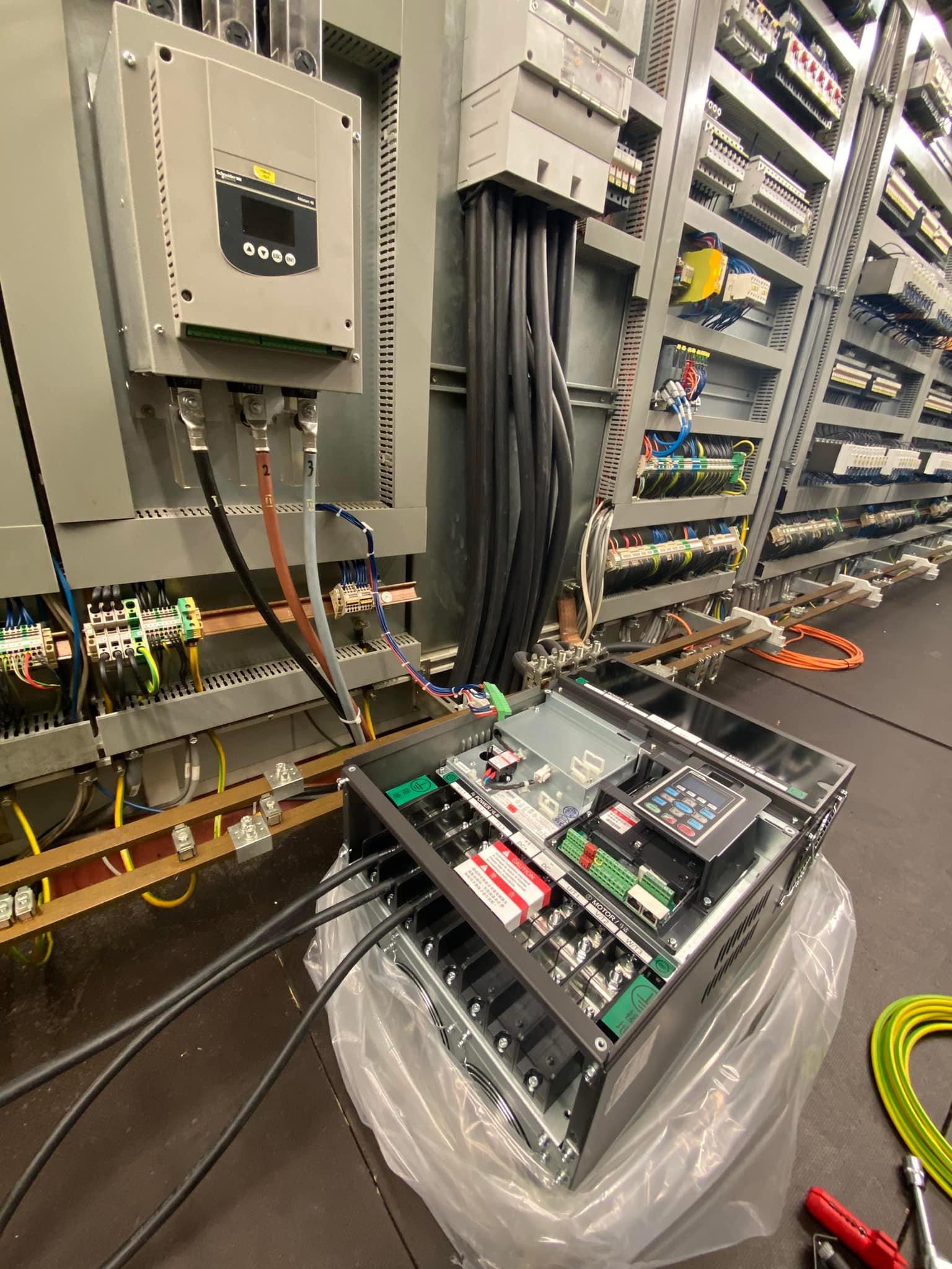 Rozbudowana szafa sterownicza z licznymi przewodami i elementami elektrycznymi, widoczne połączenia, sterowniki i zabezpieczenia, częściowo zapakowana w folię ochronną, obok leżą narzędzia.