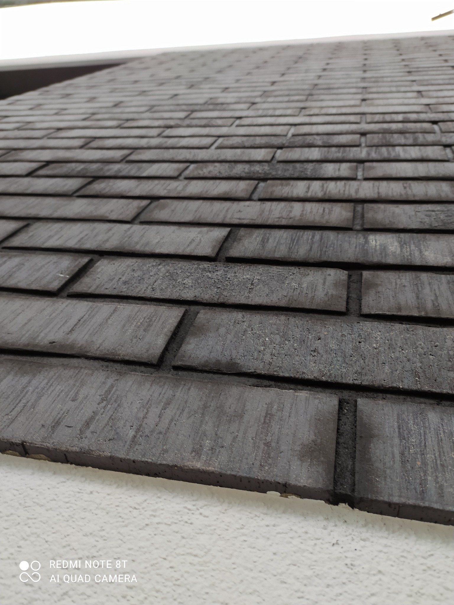 Ciemnoszare płytki klinkierowe ułożone na ścianie, widoczne z dołu pod kątem, z lekkim efektem perspektywy i widoczną fakturą.