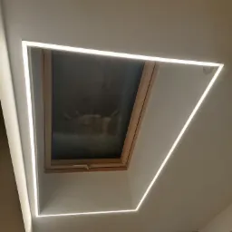 Oświetlenie LED, tworzące geometryczną ramę wokół okna dachowego, w minimalistycznym wnętrzu z jasnymi ścianami.