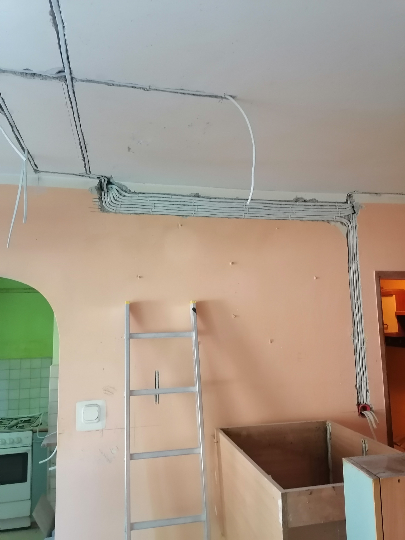Świeżo położone kable elektryczne w bruzdach na suficie i ścianie w trakcie remontu kuchni, widoczna drabina i niedokończona zabudowa meblowa.