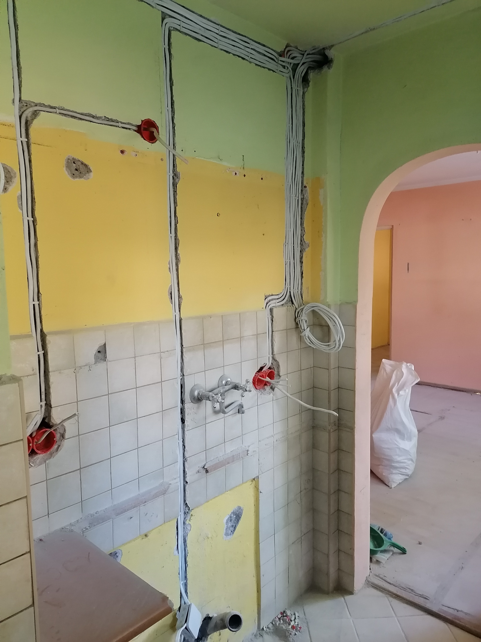 Rozprowadzenie przewodów elektrycznych w bruzdach ściennych w kuchni podczas remontu, widoczne puszki instalacyjne, białe kable ułożone wzdłuż ścian, częściowo zdjęte płytki, ściany w kolorach...