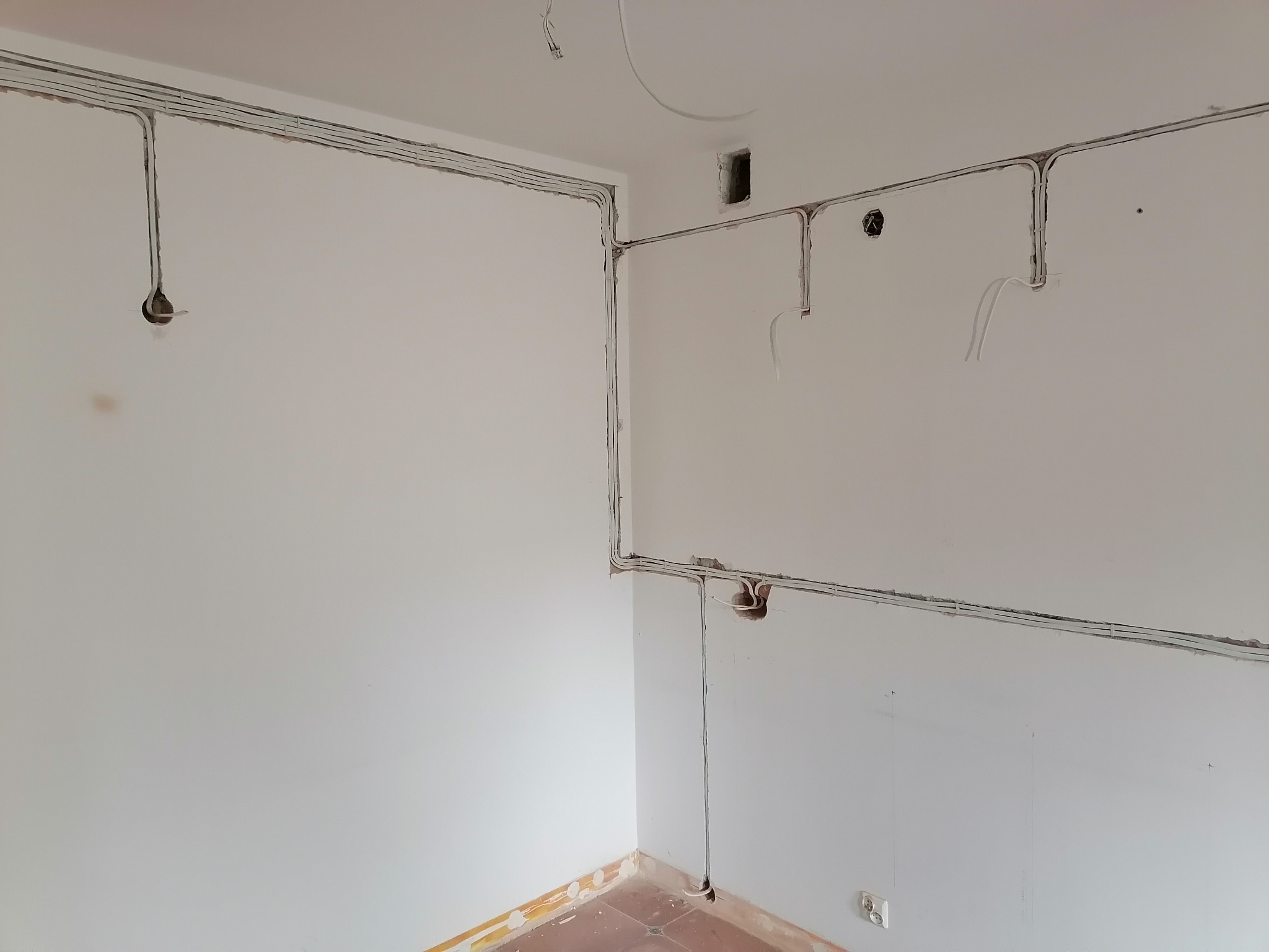 Świeżo położone kable elektryczne prowadzone w listwach na ścianach wewnątrz jasnego pomieszczenia przed tynkowaniem, widoczne puszki instalacyjne i wystające przewody.