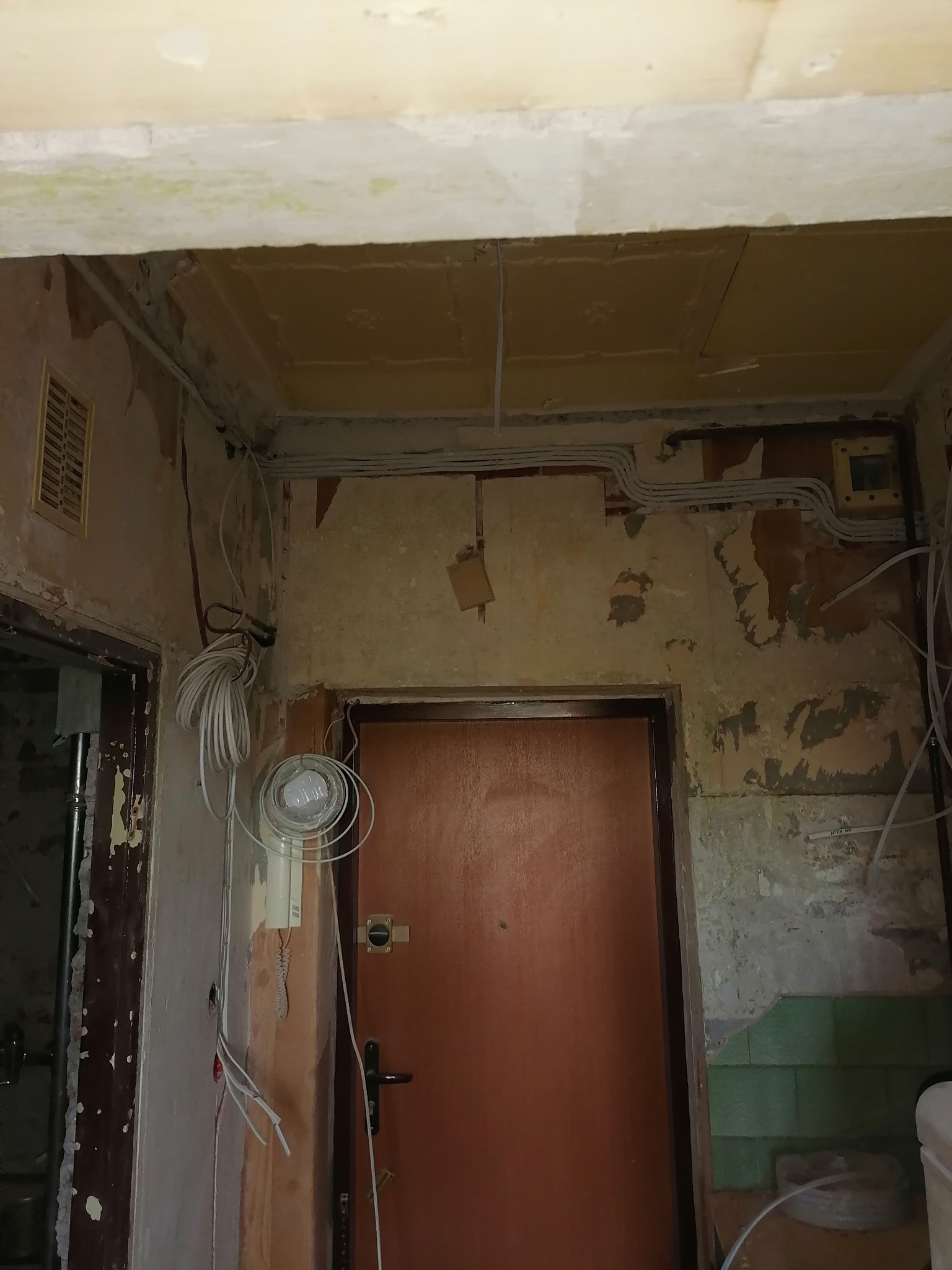 Klatka schodowa w trakcie remontu z widocznymi przewodami elektrycznymi prowadzonymi po ścianach i suficie, z fragmentami starej instalacji i elementami nowej, zniszczone ściany.