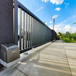 Nowoczesna, przesuwna brama w kolorze antracytowym z automatyką Somfy, widoczna na tle betonowego podjazdu i zadbanego ogrodu.