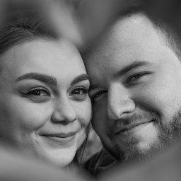 LUX-ON PHOTO Studio mobilne Katarzyna Kęsa - Czarno-białe zbliżenie twarzy uśmiechniętej pary, kadrowane w kształcie serca, z delikatnym oświetleniem podkreślającym rysy twarzy.