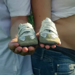 Przyszli rodzice trzymają w dłoniach parę malutkich, sportowych bucików dla dziecka, symbolizujących oczekiwanie na narodziny.