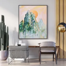 Abstrakcyjny pejzaż górski w ramie, z dominantą zieleni i pomarańczowego słońca, wiszący nad biurkiem z krzesłami w minimalistycznym wnętrzu z kaktusem.