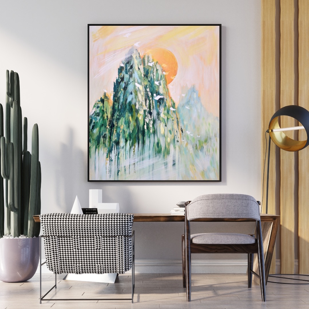 Abstrakcyjny pejzaż górski w ramie, z dominantą zieleni i pomarańczowego słońca, wiszący nad biurkiem z krzesłami w minimalistycznym wnętrzu z kaktusem.