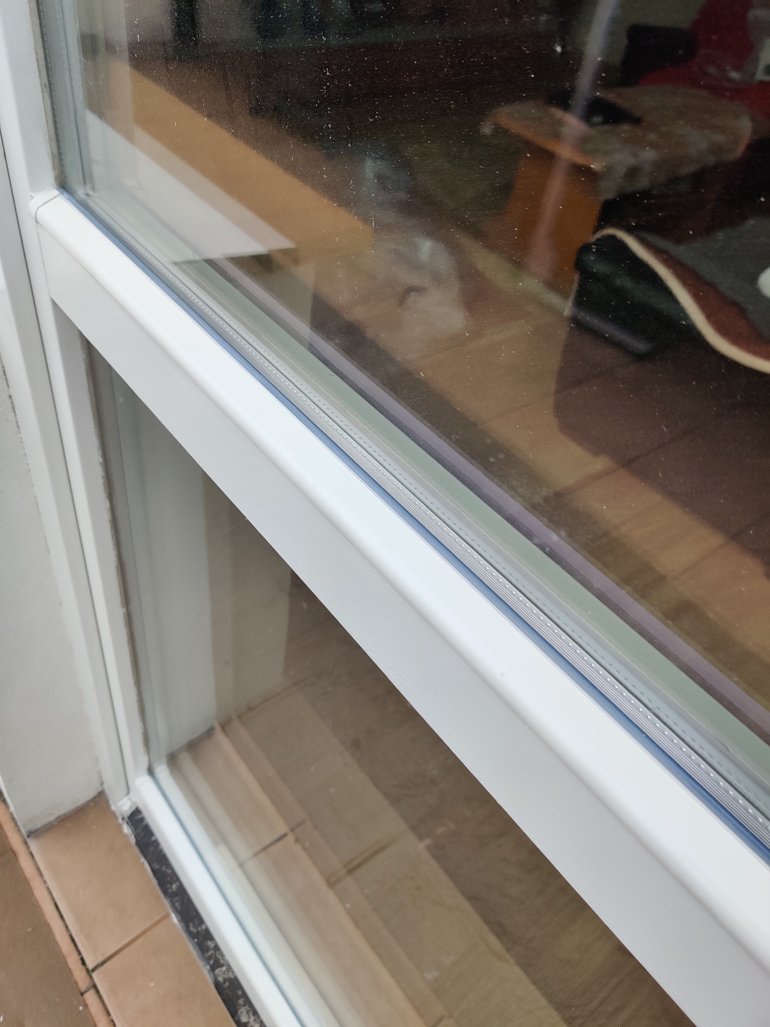 Szczegółowe ujęcie uszczelki okiennej w białej ramie okna PCV, widoczne ślady drobnych zabrudzeń na szybie, Gdańsk.