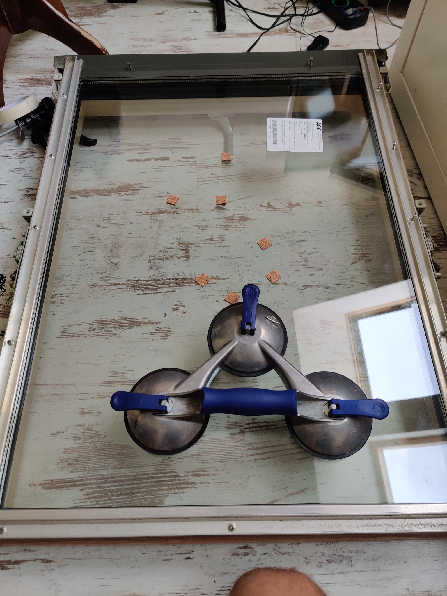 Okno w ramie, leżące na podłodze, z przyssawkami do szkła i małymi korkami zabezpieczającymi.