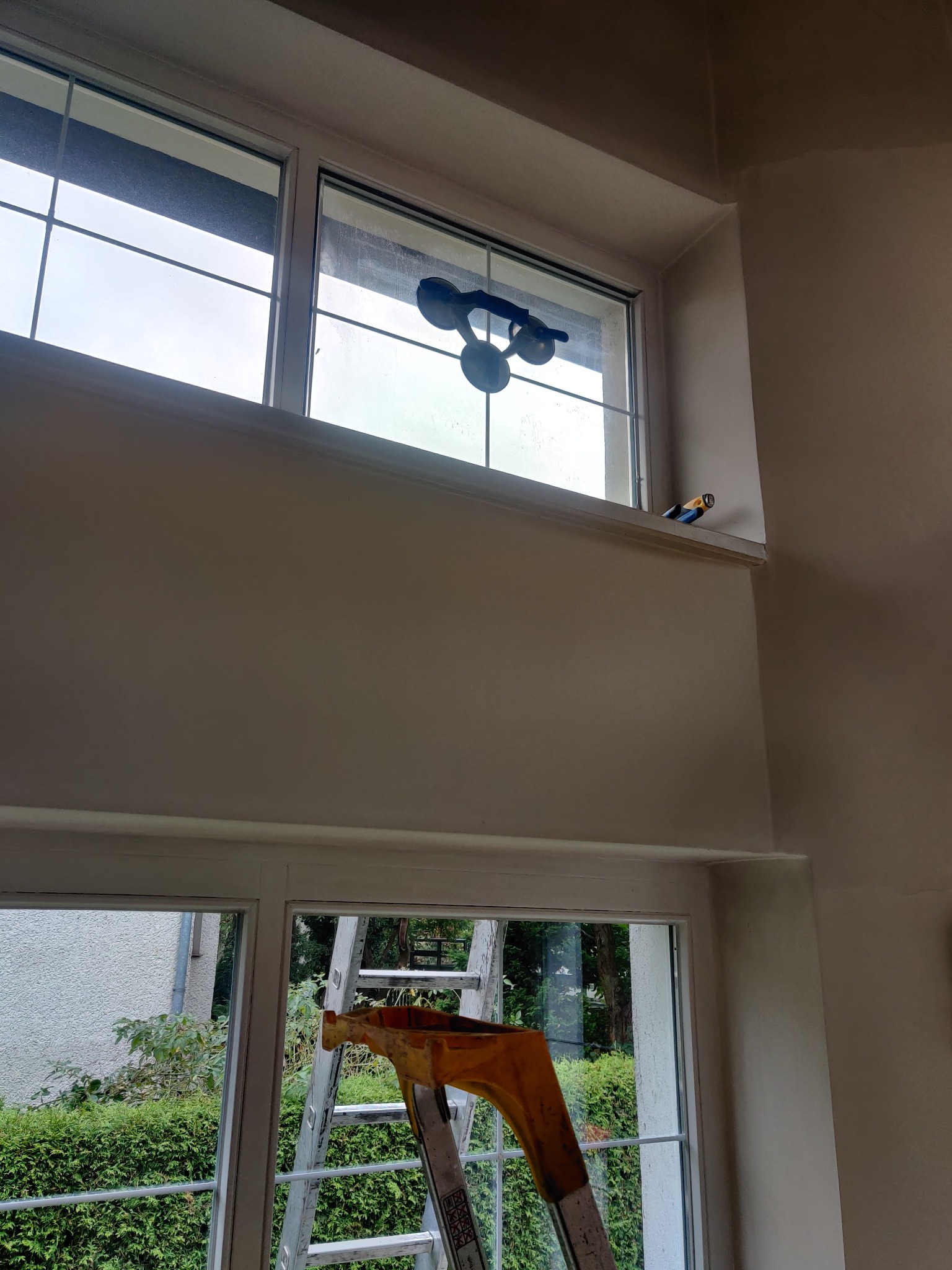 Okno z przyssawkami do szkła, drabina w tle, widok z wnętrza, etap montażu szyby.