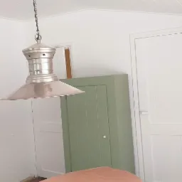 Wnętrze po odświeżeniu: białe ściany, drzwi i sufit z drewnianą boazerią, oliwkowozielona szafa w zabudowie, metalowa lampa wisząca w stylu industrialnym.