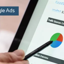 Analiza danych strony internetowej na ekranie tabletu, z widocznym wykresem kołowym i statystykami ruchu, wskazywanymi rysikiem trzymanym w dłoni, obok leży smartfon z widocznymi danymi analitycznymi.