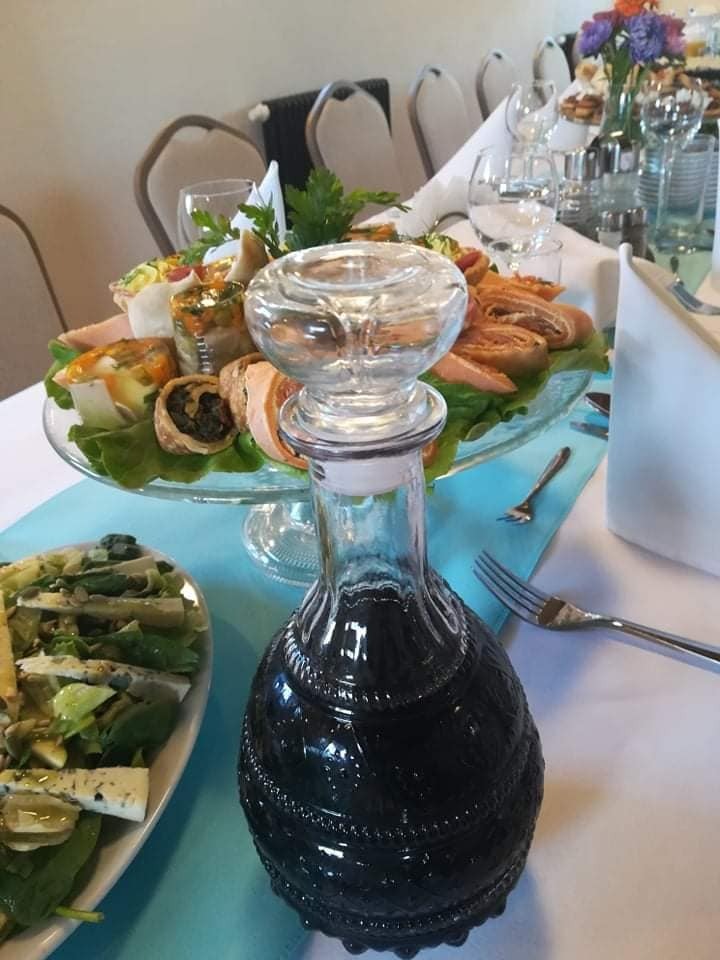 Uroczysty stół z przekąskami na paterze, sałatką i ciemną karafką z ornamentami, nakryty turkusowym bieżnikiem.