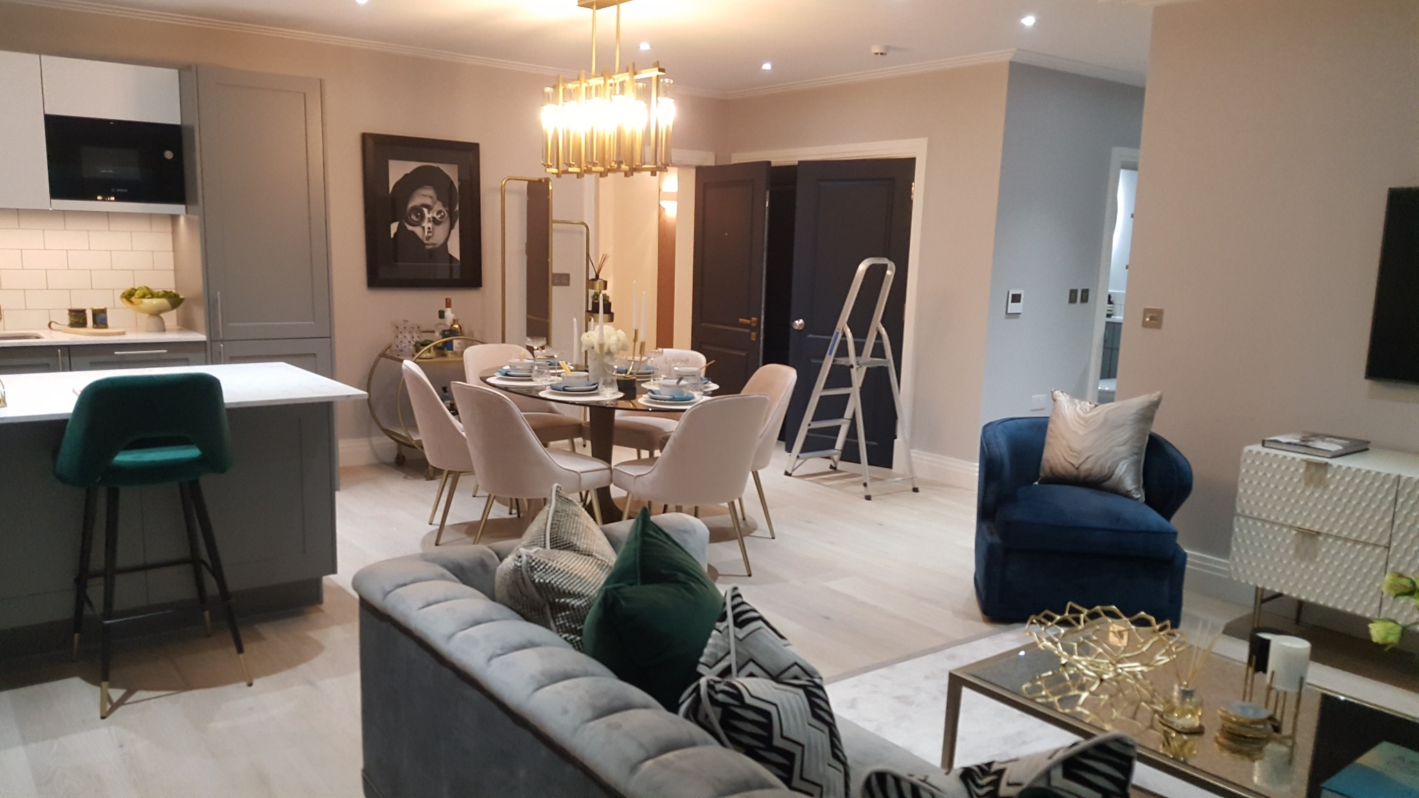 Nowoczesne wnętrze mieszkania w odcieniach szarości i beżu z elementami dekoracyjnymi, widoczna drabina oparta o ścianę, sugerująca świeżo zakończone prace.