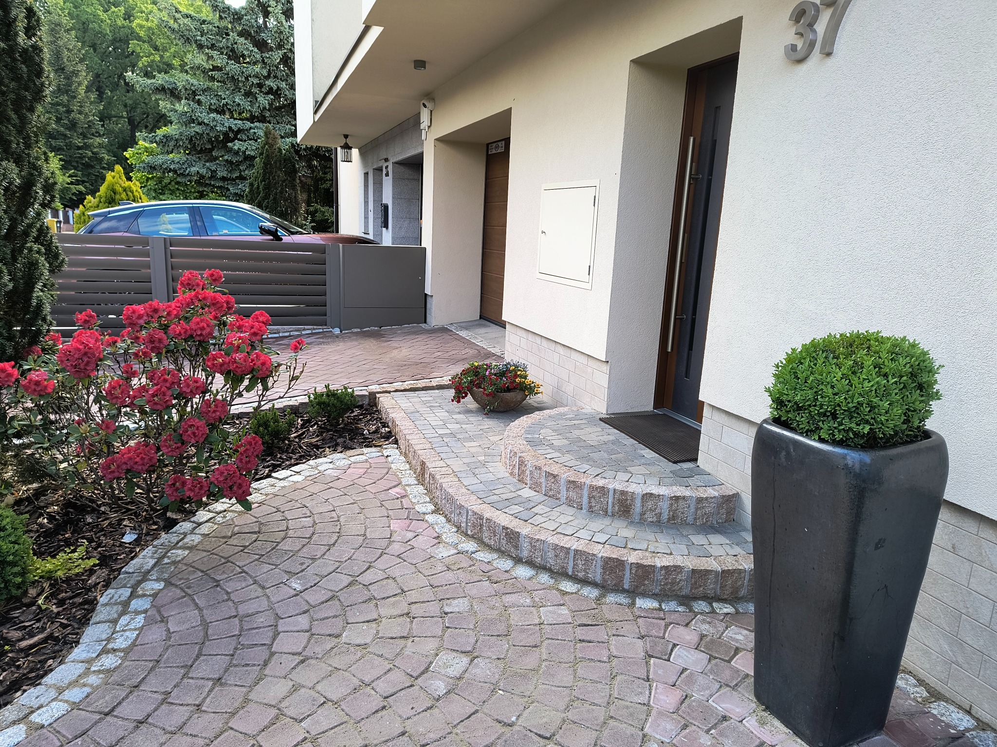 Kaskadowe schody z kostki, wzór wachlarza na brukowanej ścieżce, nowoczesny dom z szarym ogrodzeniem w tle. Detal z Borówczanej we Wrocławiu.