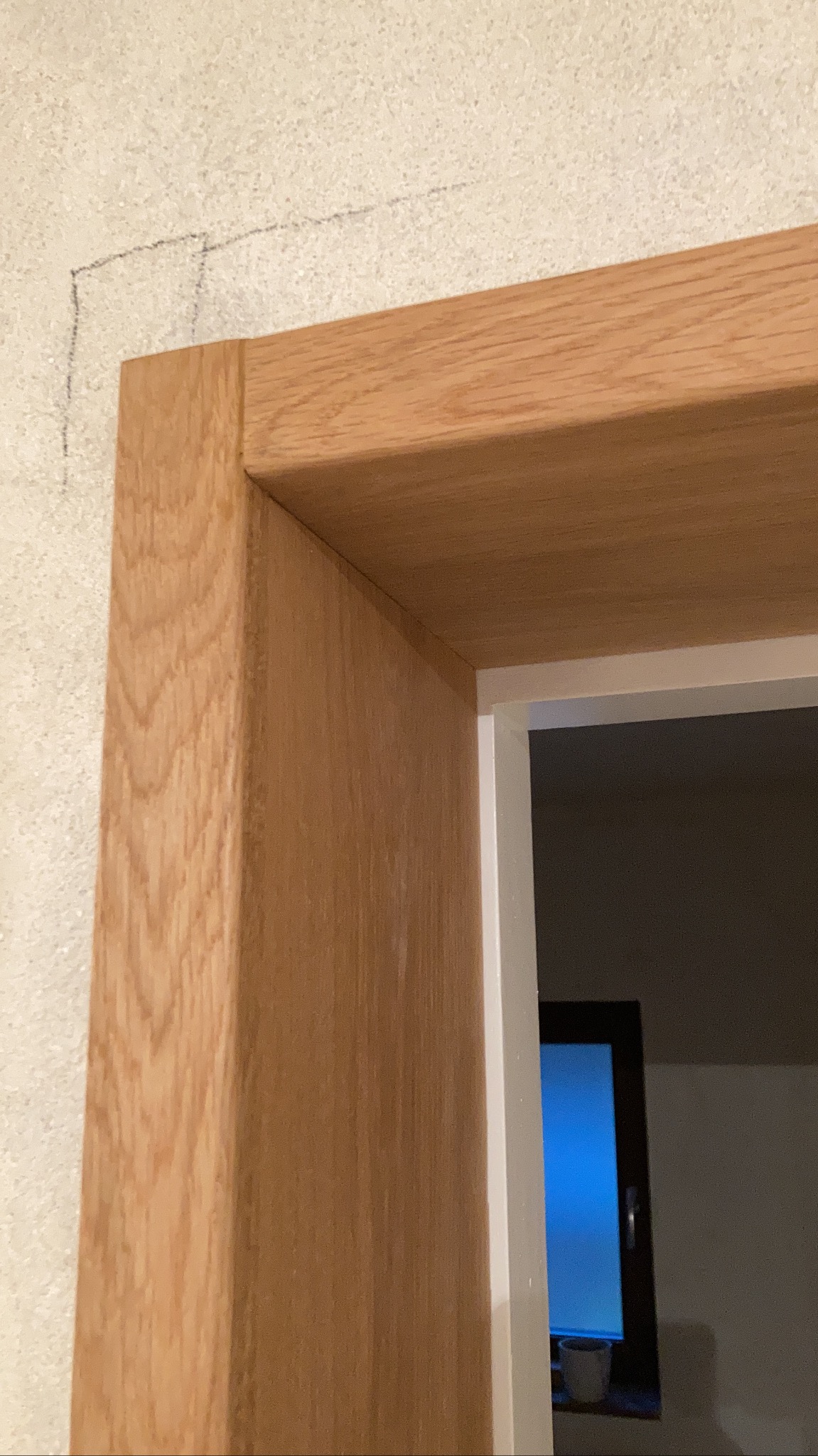 Fragment ościeżnicy dębowej w trakcie montażu, widoczne zaznaczenia ołówkiem na ścianie, surowy stan wykończenia.