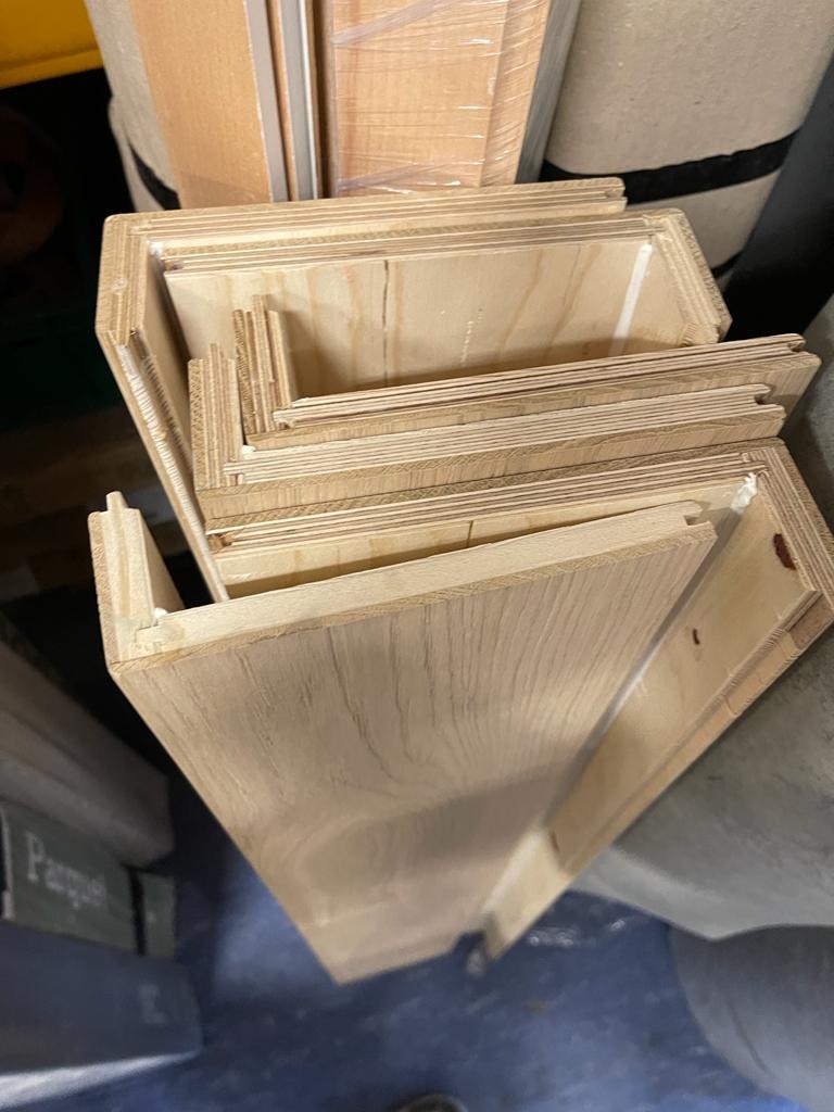 Stos wyciętych elementów drewnianych paneli podłogowych z widocznymi zamkami, oczekujących na montaż, w magazynie lub warsztacie.