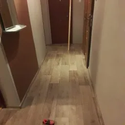 Korytarz po remoncie w Wągrowcu z nową podłogą imitującą drewno, widoczny wkrętak i poziomica na podłodze.