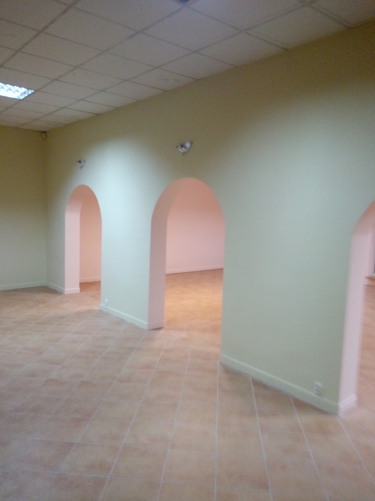 Jasne, przestronne wnętrze z łukowatymi przejściami, świeżo pomalowanymi ścianami w odcieniach beżu i terakotową podłogą, widok na kolejne pomieszczenia.