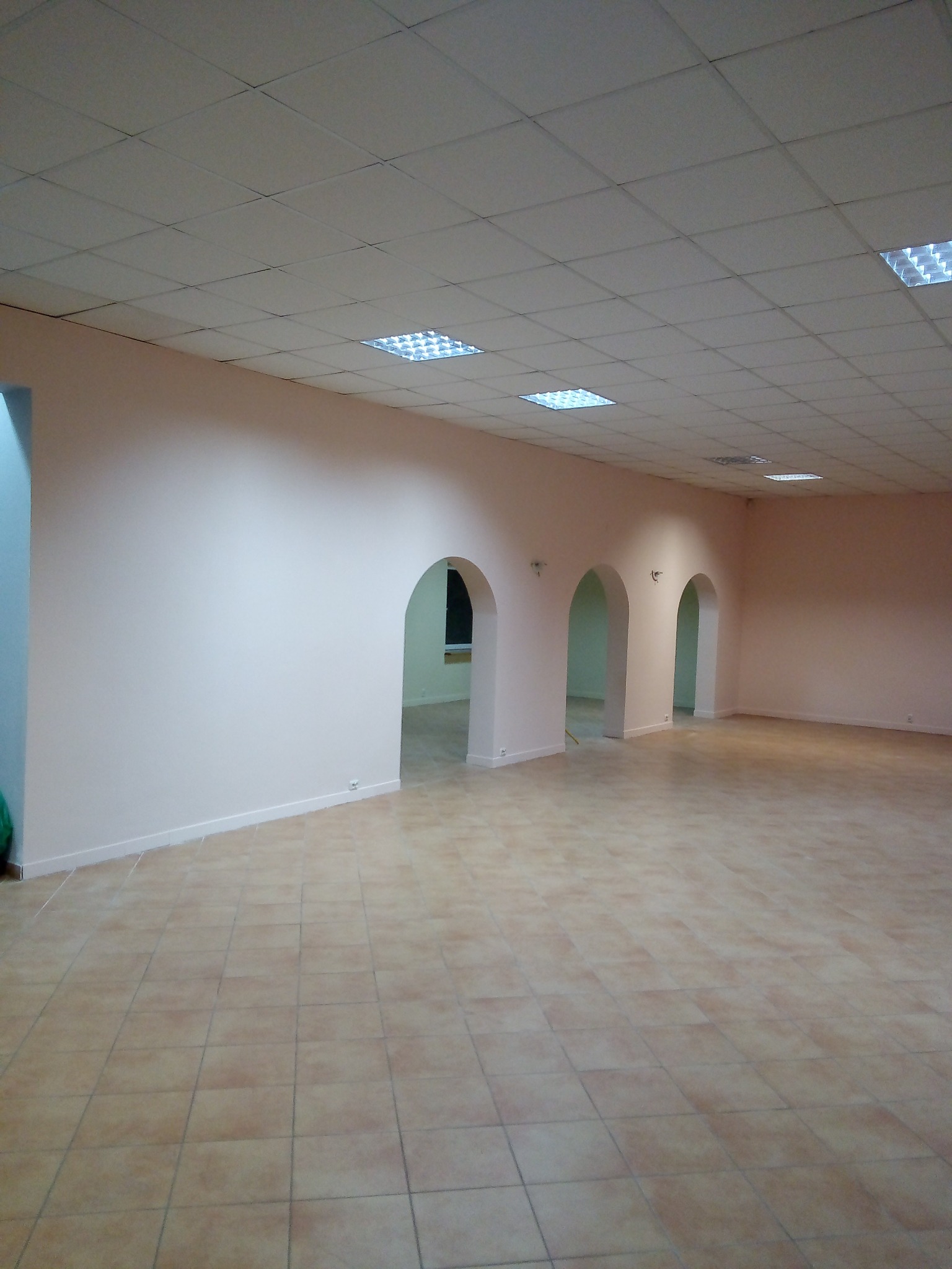 Puste pomieszczenie po remoncie z beżowymi płytkami na podłodze, łukowymi przejściami i świeżo pomalowanymi ścianami w odcieniach beżu i różu.