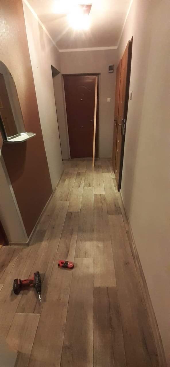 Korytarz po remoncie w Wągrowcu z nową podłogą imitującą drewno, widoczny wkrętak i poziomica na podłodze.