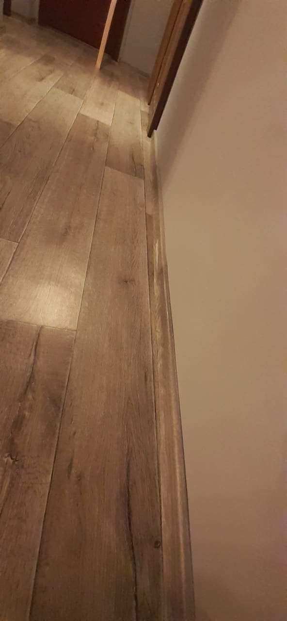 Ukończona podłoga z paneli drewnopodobnych ułożona wzdłuż ściany z widoczną listwą przypodłogową.