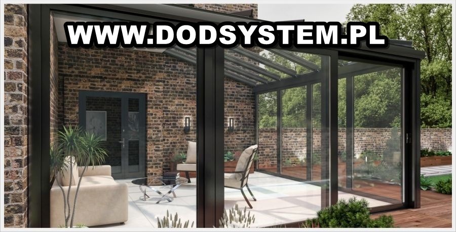 Szklana zabudowa tarasu z przesuwnymi drzwiami, czarne profile, ceglana ściana budynku w tle, widoczne meble ogrodowe i rośliny, na zdjęciu widoczny adres strony internetowej.