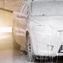 Mycie samochodu osobowego pokrytego pianą aktywną za pomocą myjki ciśnieniowej, zbliżenie na przedni reflektor i koło.