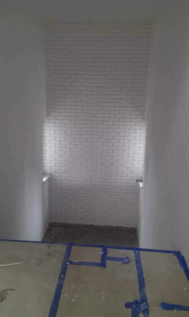 Świeżo wykończona ściana z białej cegły w wąskim korytarzu w Wejherowie, zabezpieczona podłoga z widoczną taśmą malarską, ukazująca etap prac wykończeniowych.