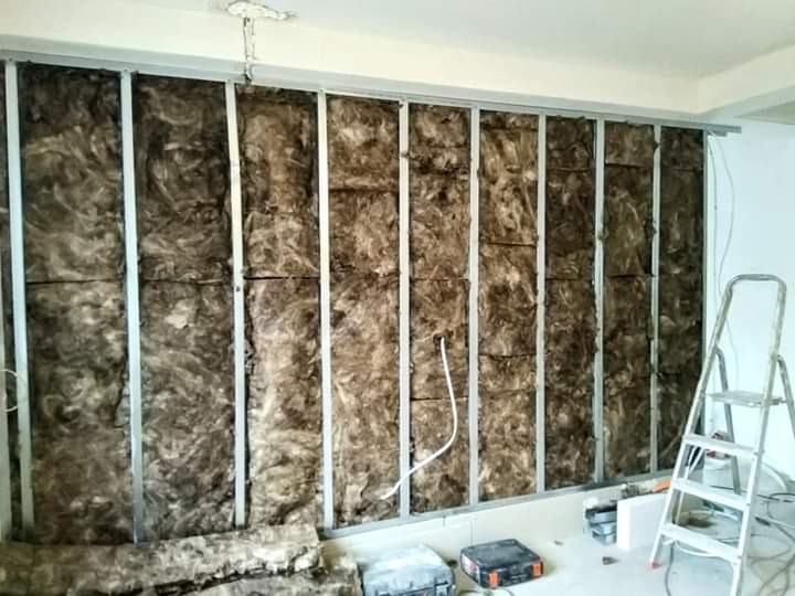 Ściana wewnętrzna z metalowym stelażem wypełnionym brązową wełną mineralną, częściowo zakryta, widoczna drabina i narzędzia na podłodze.