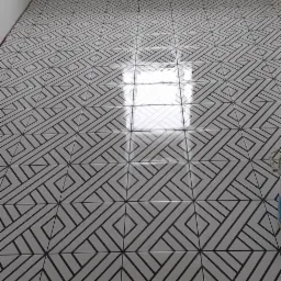 Ułożona podłoga z białych płytek ceramicznych z geometrycznym wzorem w czarnych liniach, widok na fragment pokoju z oknem i grzejnikiem.