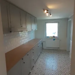 Jasna kuchnia po remoncie: szare szafki z drewnianym blatem, białe płytki na ścianie i wzorzysta podłoga z geometrycznym deseniem.