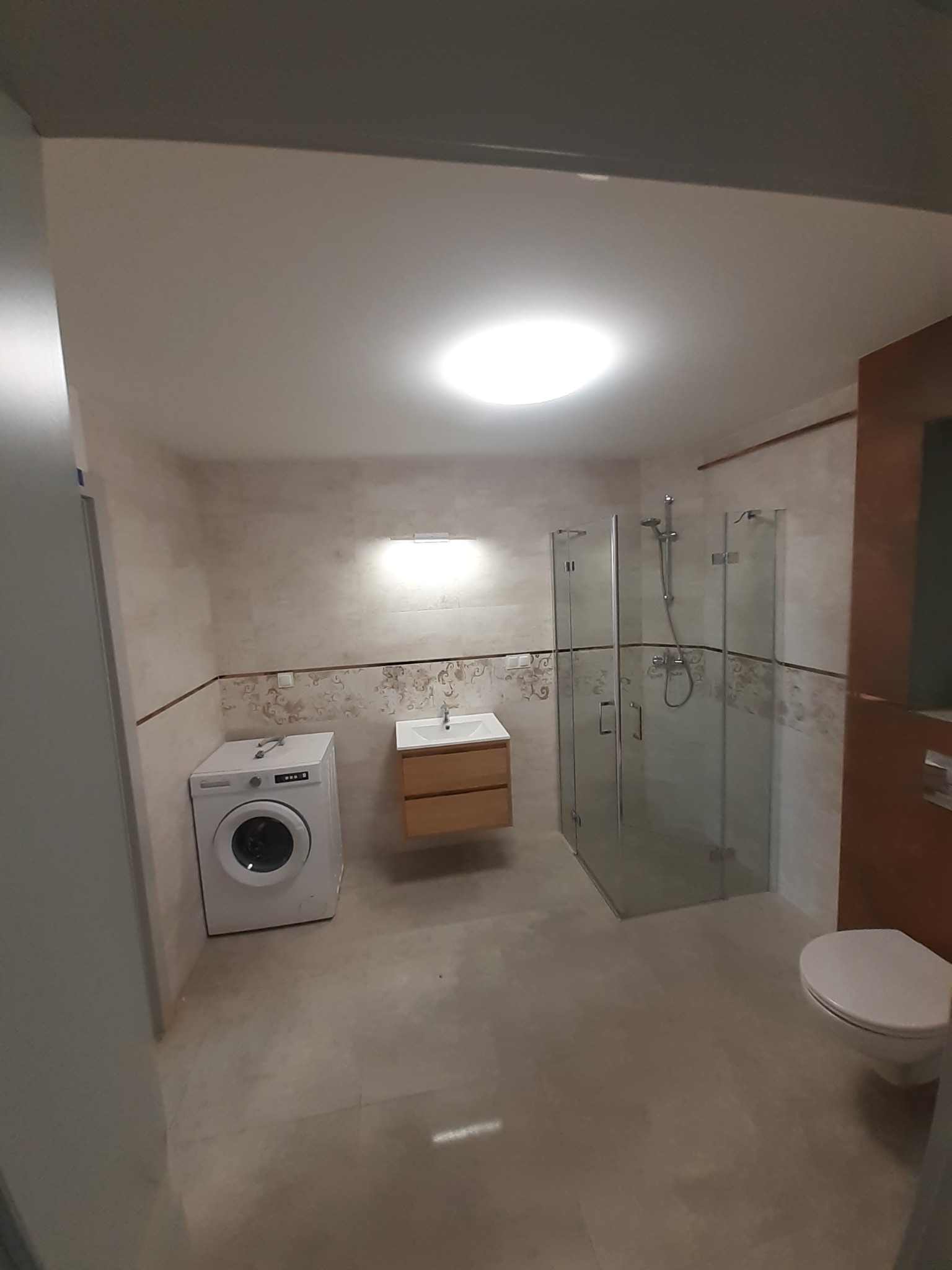 Wykończona łazienka w Chmielnie z kabiną prysznicową, umywalką z szafką, toaletą i pralką. Na ścianach dekoracyjne płytki.