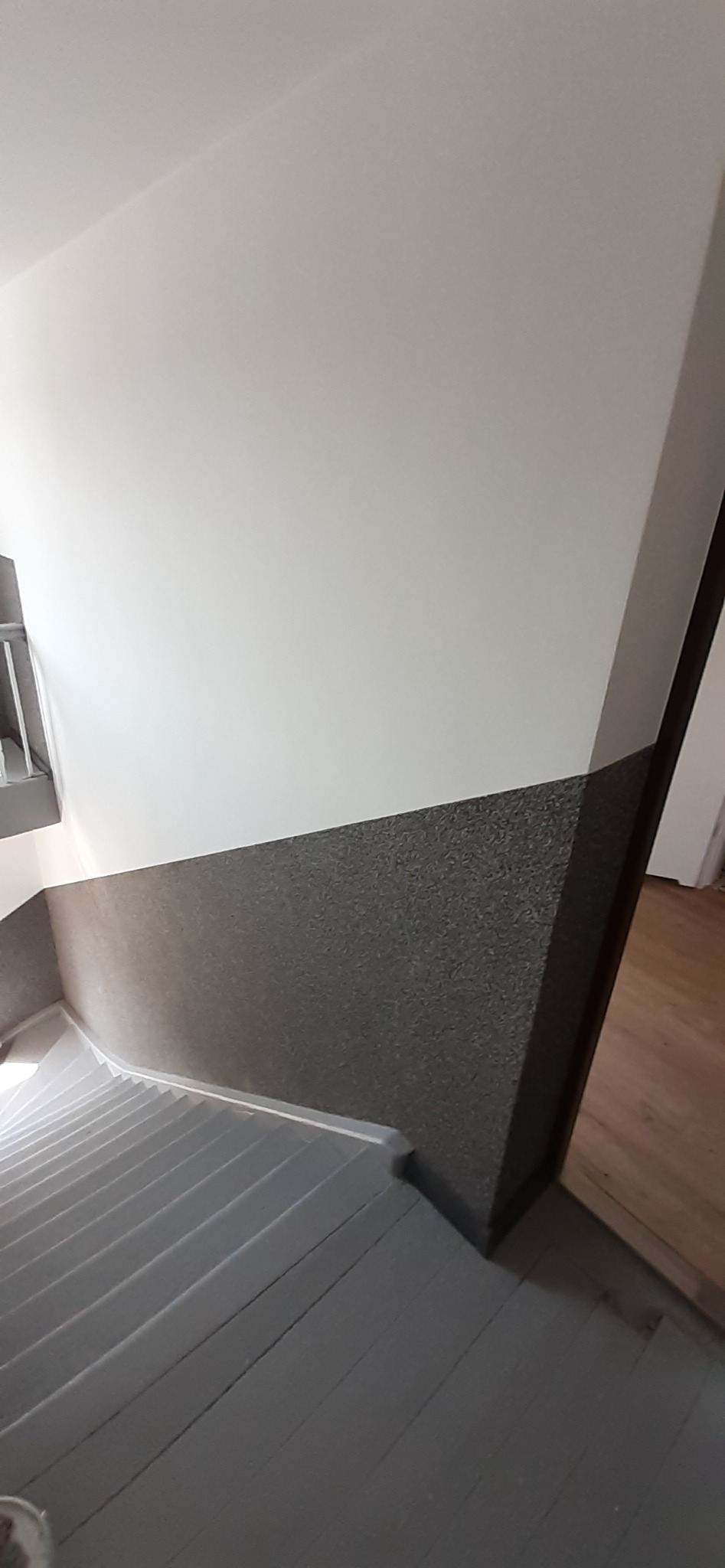 Klatka schodowa po odświeżeniu: szare, drewniane schody i ściany z dwukolorowym wykończeniem, biała góra i ciemnoszara faktura na dole.