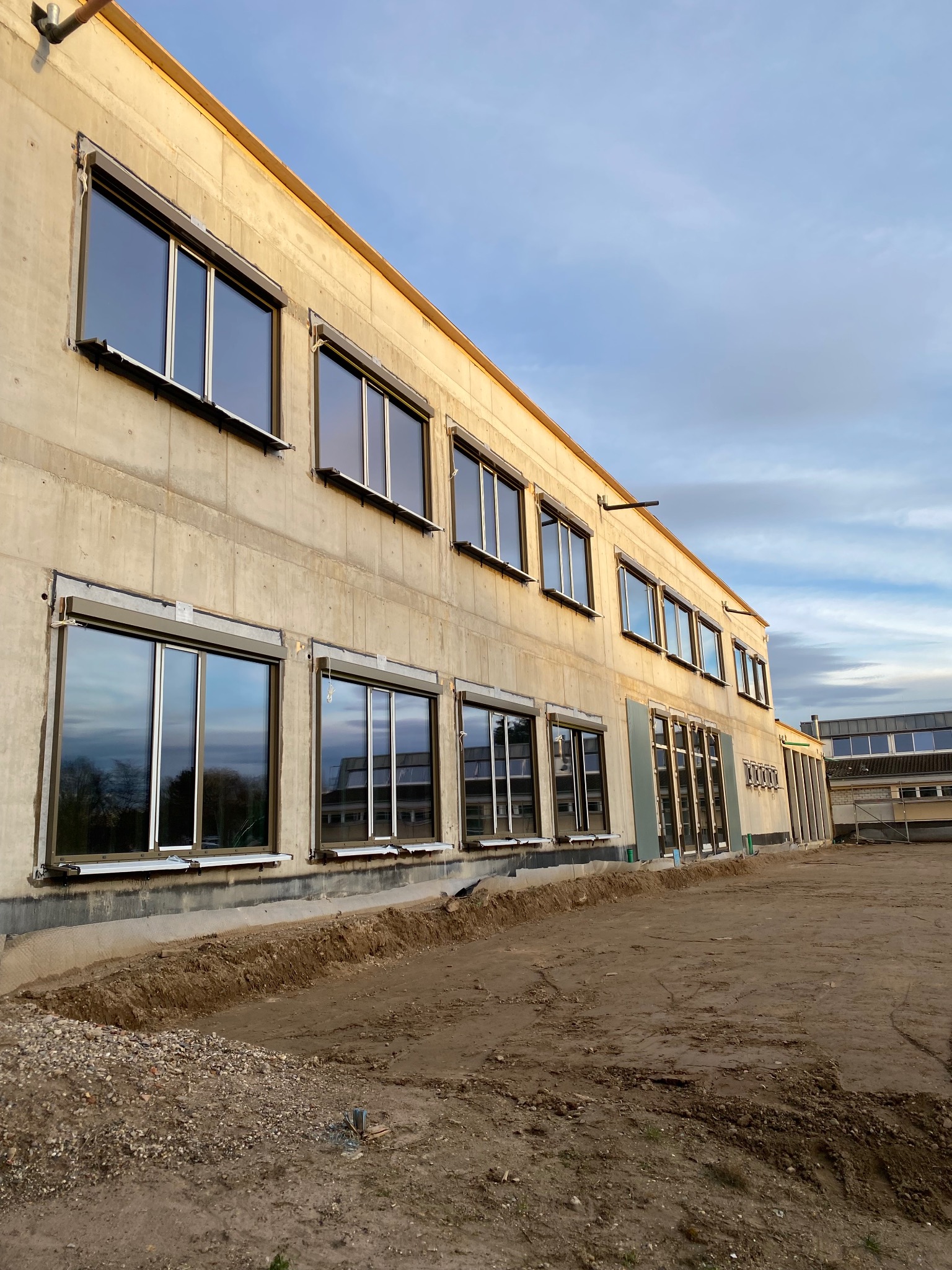 Nowo zamontowane okna z szarymi ramami w surowym budynku w Padwi Narodowej, widok z zewnątrz, teren wokół budynku w trakcie prac ziemnych.