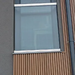 Okna z aluminiowymi ramami w nowoczesnym budynku z drewnianą fasadą i szarym tynkiem.