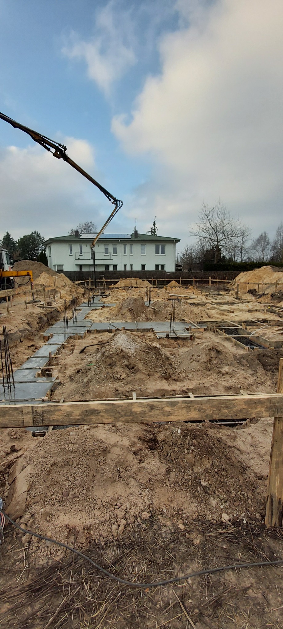 Wylewanie fundamentów pod budynek jednorodzinny z użyciem pompy do betonu, widoczne zbrojenia i szalunki.