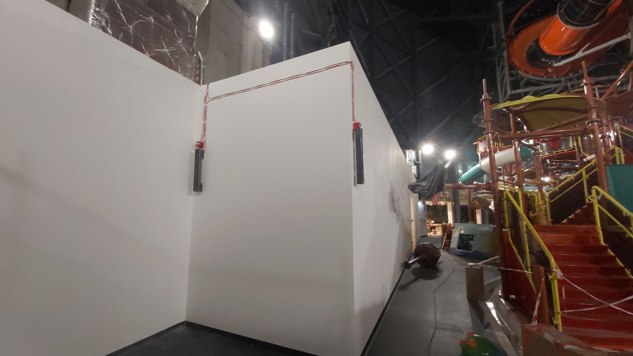 Biała ściana z wyprowadzonymi kablami i czujnikami przeciwpożarowymi, w tle konstrukcja aquaparku z rurami i schodami.