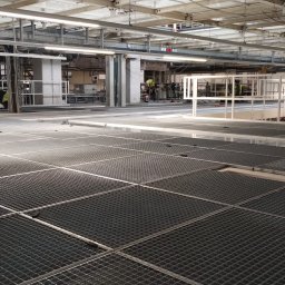 Iron Workers Sp. z o.o. - Szeroki kadr na metalową kratownicę podłogową w hali przemysłowej, z widocznymi elementami konstrukcji stalowej i pracującymi osobami w tle.