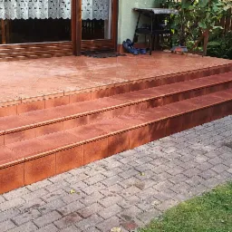 Wykończone płytkami schody wejściowe do domu z widocznym workiem zaprawy Atlas na trawniku obok.