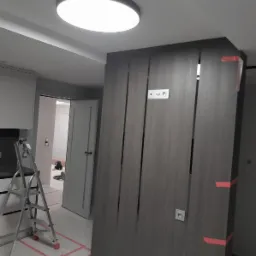 Montaż ścianki działowej z płyty karton gips z widocznymi pionowymi szczelinami dekoracyjnymi, zabezpieczona taśmą malarską, na podłodze widoczne ślady po wyznaczaniu położenia, drabina w tle.