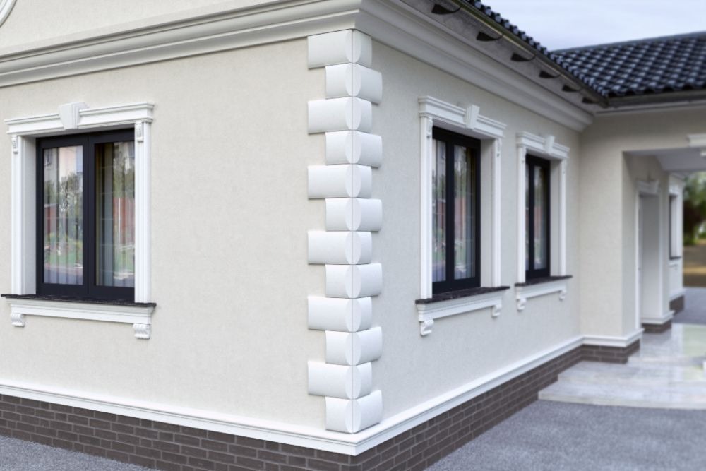 Elewacja budynku z dekoracyjnymi elementami narożnymi i ozdobnymi obramowaniami okien w kolorze białym. Dolna część elewacji wykończona cegłą.