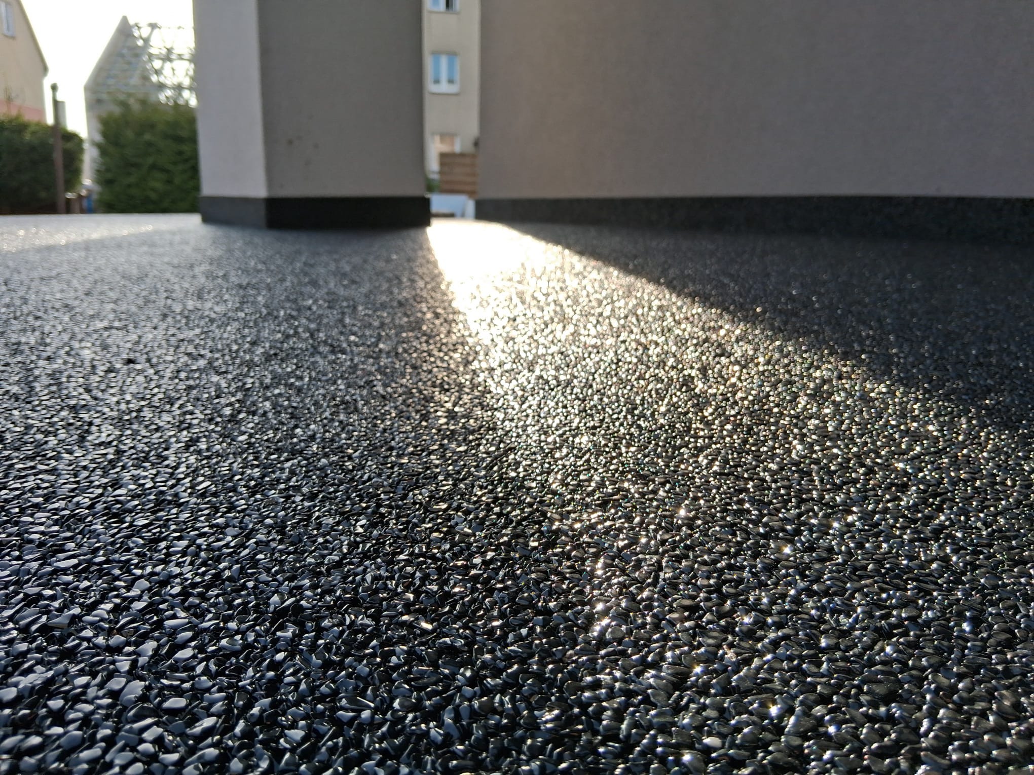 Błyszcząca, czarna, żywiczna posadzka balkonu w promieniach słońca, z fragmentem elewacji budynku w tle. Unikalna faktura i gra świateł.