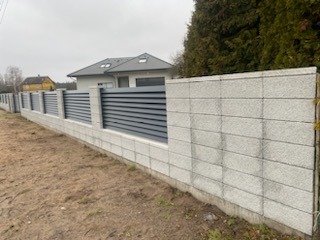 Nowoczesne ogrodzenie z szarego betonu architektonicznego i poziomych paneli w Kleosinie. Minimalistyczny design, widok z bliska, jesienna sceneria.