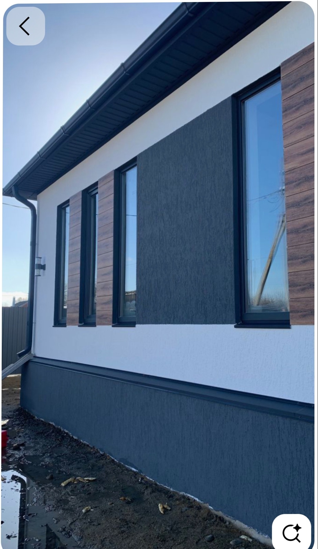 Nowoczesna elewacja domu jednorodzinnego z elementami dekoracyjnymi imitującymi drewno, ciemnoszara struktura tynku i białe wykończenia. Widoczne okna z czarnymi ramami.