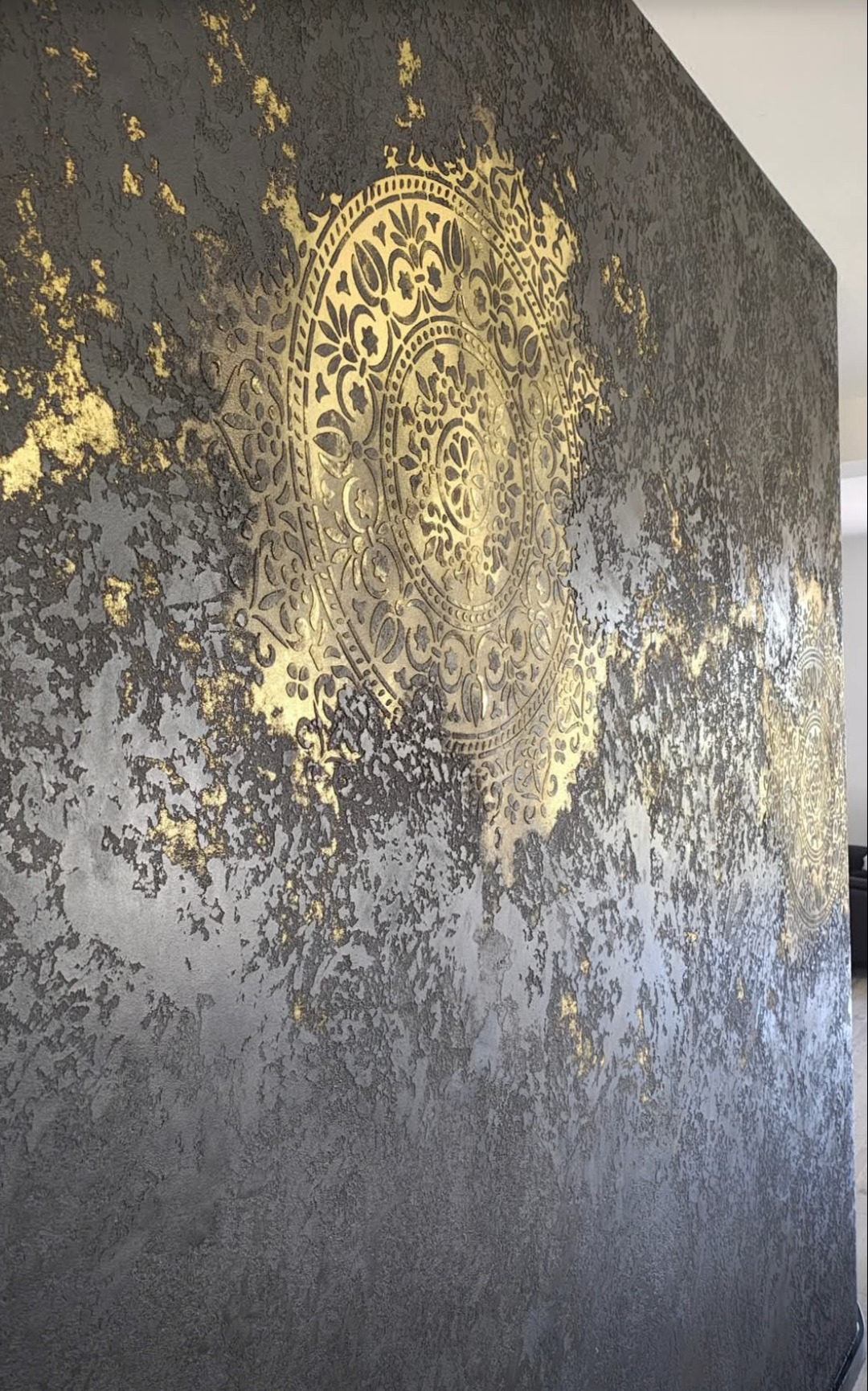 Dekoracyjna ściana w odcieniach szarości z wyraźną fakturą i złotymi, okrągłymi ornamentami. Efektowna gra światła podkreśla unikalny wzór i strukturę.