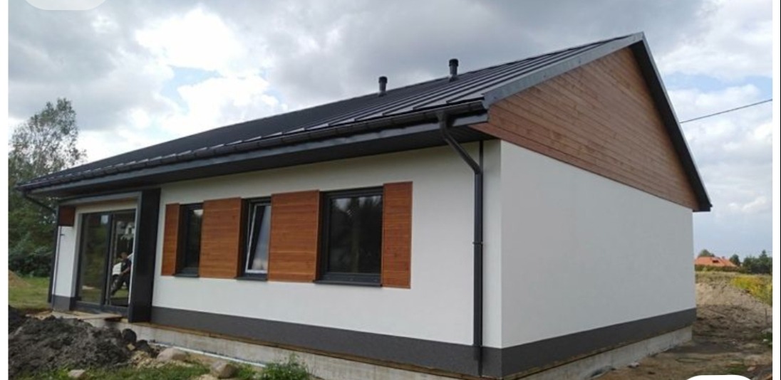 Wykończony dom jednorodzinny z drewnianymi okiennicami i elewacją w odcieniach bieli i szarości, widoczny z zewnątrz w pochmurny dzień.